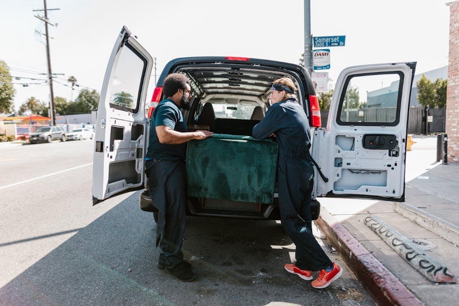 Two people putting a green velvet box at the back of a truck