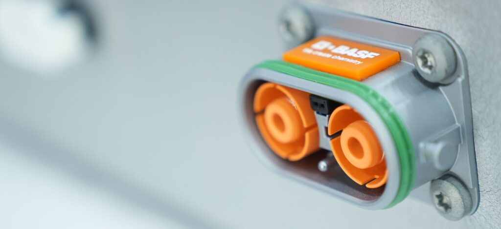 A BASF electrical connector featuring two orange power terminals and a locking mechanism, with a metallic housing bolted to a panel.